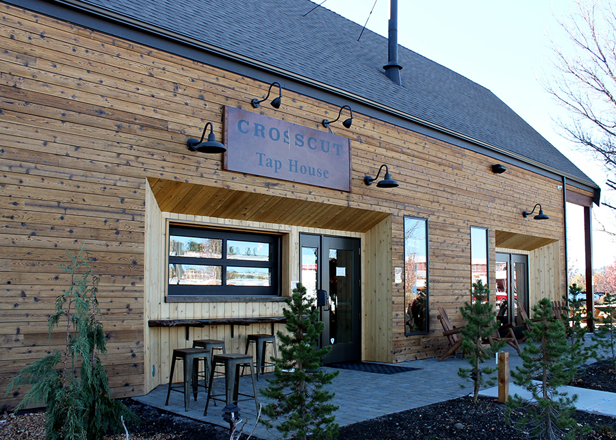 The street-side of the tap house, the timber construction at the forefront, Adirondack chairs sit around the fireplace 